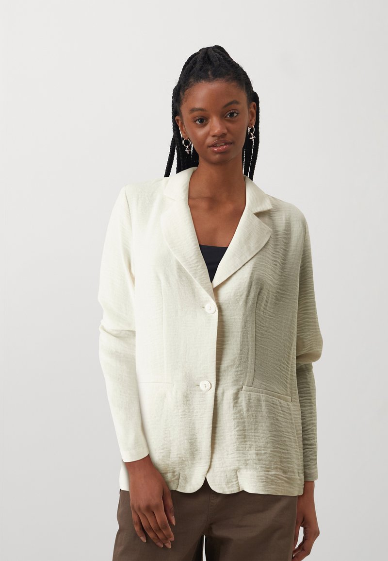 Cream-colored blazer made of textured fabric, featuring a notched collar, single-button closure, and front pockets. Scalloped hem detail.