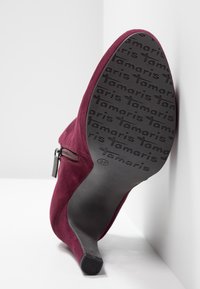 Bottine pour femme en daim bordeaux avec une fermeture éclair et une semelle noire affichant la marque répétée "tamaris" ainsi que la taille 37.