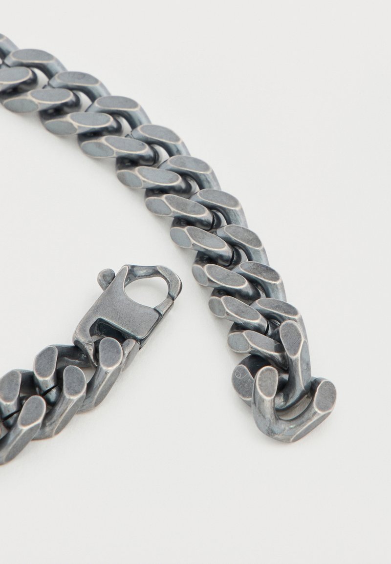 Bracelet chaîne en métal de ton argenté ; présente des maillons ovales entrelacés et une fermeture à fermoir ; surface lisse avec un léger éclat et bords arrondis.