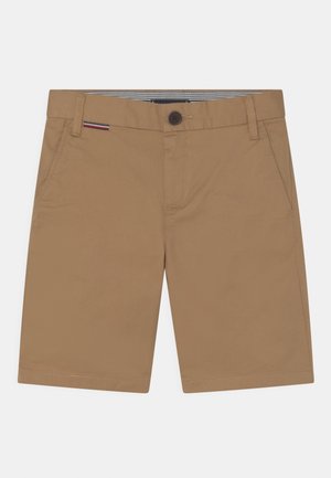 Knælange shorts i tan-farve med forlommer, bæltestropper, knaplukning og et lille rødt, hvidt og sort stribet mærke nær taljen.