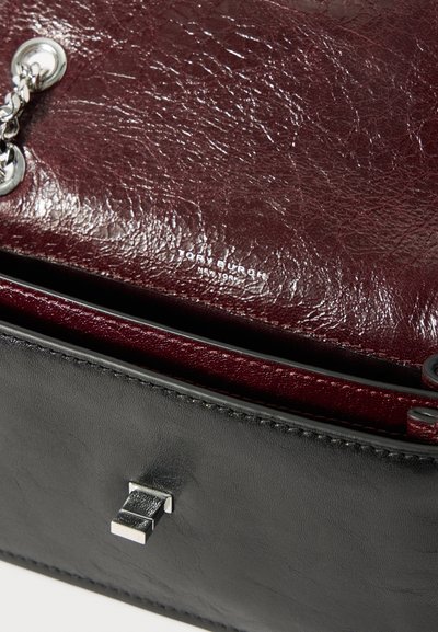 Ανοιχτή μαύρη δερμάτινη τσάντα χειρός με μπορντώ υφή στο εσωτερικό και ασημί αλυσίδα, το λογότυπο Tory Burch New York ορατό μέσα.