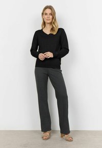 Maglione nero a collo a V con maniche lunghe, abbinato a pantaloni a gamba larga grigio scuro a righe e sandali con tacco strappy color taupe.
