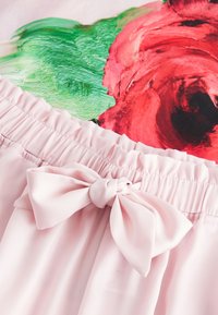 Rok aus pinkem Satin mit einem gerafften Bund und einer Schleifendetails an der Vorderseite, vor einem bunten floralen Hintergrund.