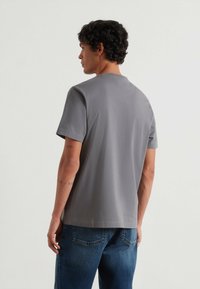 Graues Kurzarmhemd mit lässiger Passform, glatter Textur und Rundhalsausschnitt, kombiniert mit blauen Denim-Jeans.