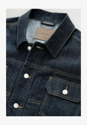 Tume sinine teksajakk terava kraega, hõbedaste riidest nööpidega, kahe rinnataskuga ja nahklabeliga, millel on kiri "DENIM SUPPLY."