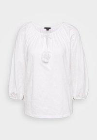 Biała bluzka z bufiastymi rękawami i okrągłym dekoltem. Posiada marszczony materiał wokół szyi oraz wiązanie z puszystym pomponem.