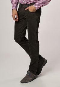 Donkerbruine broek van zacht materiaal, met een mooie pasvorm, zijzakken en subtiele stikdetails. Gepaard met grijze schoenen.