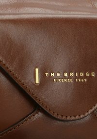 Braune Ledertasche mit glatter Oberfläche, genähten Details und einem goldenen eingeprägten Logo mit der Aufschrift "THE BRIDGE FIRENZE 1969."