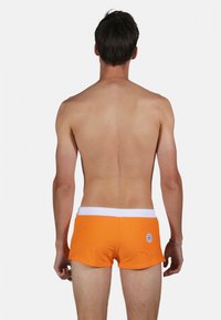 Shorts de bain orange avec une taille blanche, conçus avec une poche arrière arborant un détail de logo circulaire, texture de tissu lisse.