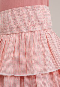 Roza gingham večslojna krila s smokanjem v pasu. Tkanina je lahka s teksturiranim volančkom ob robu.