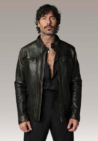 Veste en cuir noir avec un design ajusté, zips proéminents et col montant ; présente une finition texturée et des surpiqûres contrastantes.