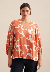Blusa a maniche lunghe con un motivo floreale rosa e bianco, caratterizzata da una scollatura a V, maniche arricciate e una vestibilità morbida. Tessuto liscio e leggero.
