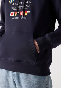 Felpa navy con tasca a marsupio frontale, polsini e orlo a costine, decorata con grafiche ricamate e dettagli del logo legati alla vela.