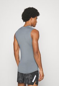 Graues ärmelloses Sportshirt aus elastischem Stoff, enganliegendes Design, das Schultern und Arme betont, kombiniert mit schwarzen gemusterten Shorts.