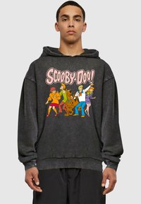 Felpa nera con cappuccio caratterizzata da un vivace grafica di "Scooby-Doo!" con i personaggi: Velma, Shaggy, Scooby, Fred e Daphne. Morbido al tatto, vestibilità comoda.