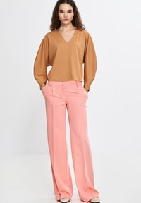 Brązowa bluzka w serek z bufiastymi rękawami, połączona z różowymi szerokimi spodniami z dwoma przednimi guzikami. Gładka faktura materiału.