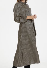 Lång svart och vit klänning med polka prickar, krage, knappstängning och långa ärmar. Tillverkad av ett glatt tyg med en flödande design.