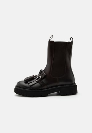 Stivaletto alla caviglia in pelle nera con suola robusta, pannelli laterali elastici e decorazioni con nappine sulla parte anteriore, mostrato su sfondo bianco.