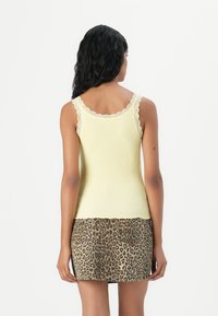 Débardeur jaune à côtes avec bord en dentelle, associé à une jupe en denim imprimé léopard. Vue arrière mettant en avant la texture du tissu et l'ajustement.
