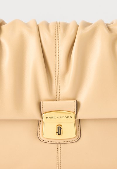 Μπεζ δερμάτινη τσάντα Marc Jacobs με σούρα στην πάνω πλευρά και κούμπωμα σε χρυσό τόνο με το όνομα και το λογότυπο της μάρκας.