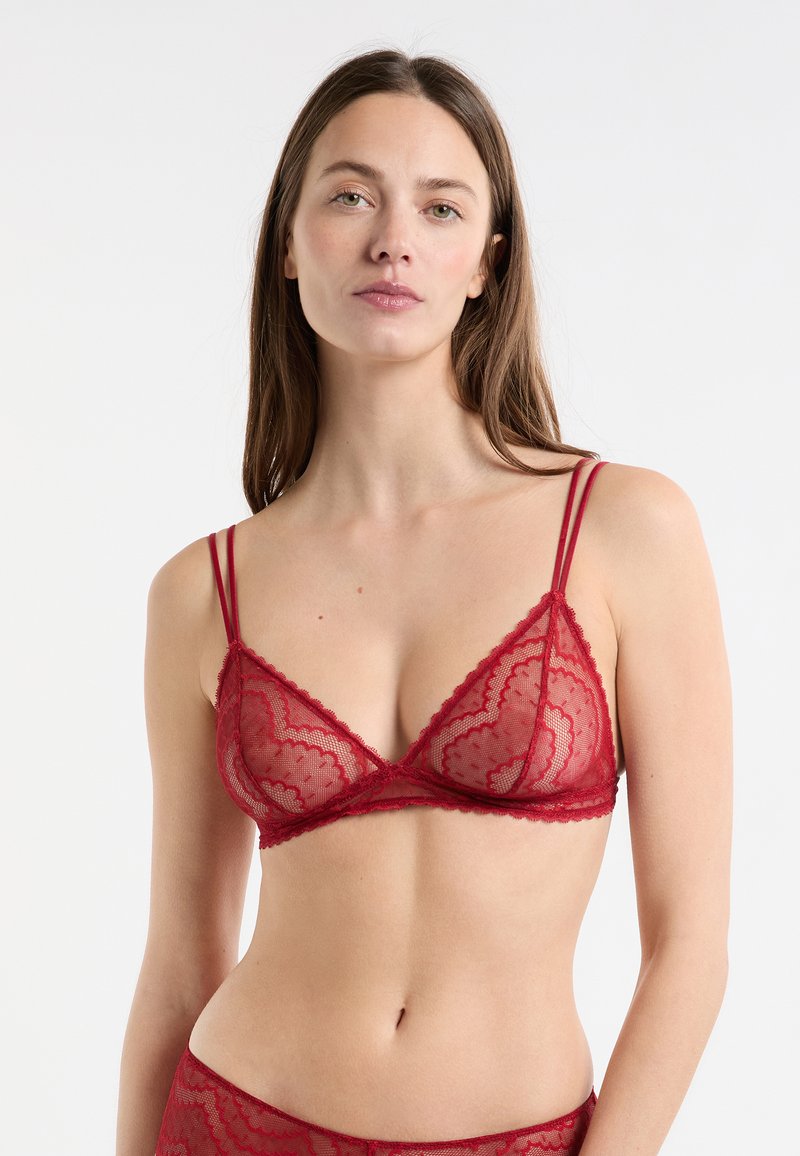 Red lace bralette with thin adjustable straps, featuring scalloped edges and a triangular design. Sheer texture with floral pattern details.