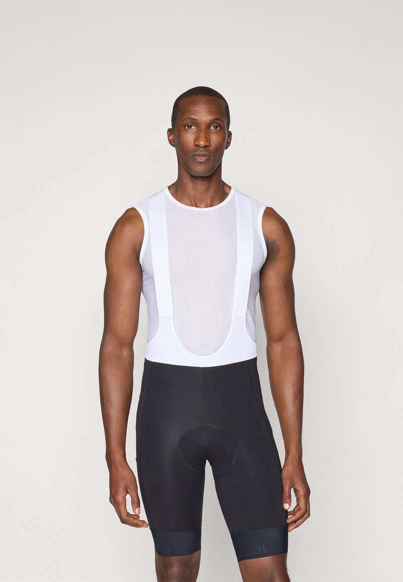 T-shirt de base en maille blanche pour le cyclisme associé à un short rembourré noir. Présente un col rond, un design sans manches et un tissu texturé.