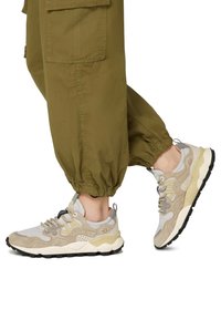 Sneakers leggeri di colore beige, con tomaia in suede e mesh, suola ammortizzata, battistrada nero e cuciture decorative. Abbinati a pantaloni elastici verde alla caviglia.