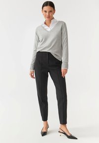 Grå v-hals sweater over en hvid skjorte med krave, parret med sorte skræddersyede bukser og sorte slingback-sko med en guld-accent.