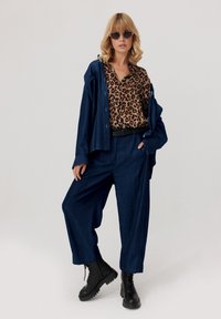 Jeansowa koszula i spodnie o szerokich nogawkach w ciemnoniebieskim kolorze, zestawione z bluzką w panterkę. Czarny pasek i buty wojskowe dopełniają całość.