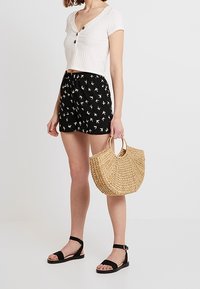 Top court côtelé blanc avec des boutons ; short noir avec imprimé oiseaux blancs ; sac à main en osier ; sandales noires à lanières avec bride de cheville.