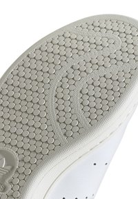 Suola di scarpa in gomma bianca con motivo di presa circolare e linee curve testurizzate per la trazione.