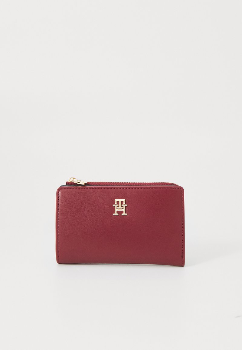 Portefeuille en cuir bordeaux avec quincaillerie dorée, de forme rectangulaire, fermeture éclair, détail de logo embossé à l'avant, texture lisse.