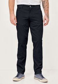 Marineblaue Chinos mit geradem Beinschnitt, ausgestattet mit Vordertaschen, einem Reißverschluss und dezenten Nähdetails. Kombiniert mit blauen Freizeit-Sneaker.