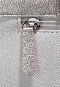 Materiale bianco texturizzato con un’apertura a zip metallic silver. La zip ha una finitura lucida ed è posizionata vicino a un accento con un motivo geometrico.