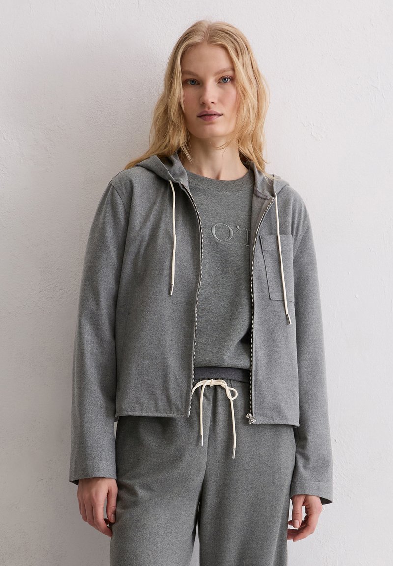 Szara bluza z kapturem zapinana na zamek, z troczkami i przednią kieszenią, zestawiona z szarą koszulką z okrągłym dekoltem, prezentowana na modelu.