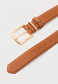 Tan-värinen nahkavyö, jossa on kultarectangulaarinen solki, yhteensopiva silmukka ja pieni pyöreä kultakoriste soljen päässä.