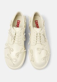 Scarpe in pelle color crema con dettagli a fiocco, design con lacci, forma arrotondata e suola texturizzata. L'interno presenta lettere rosse.