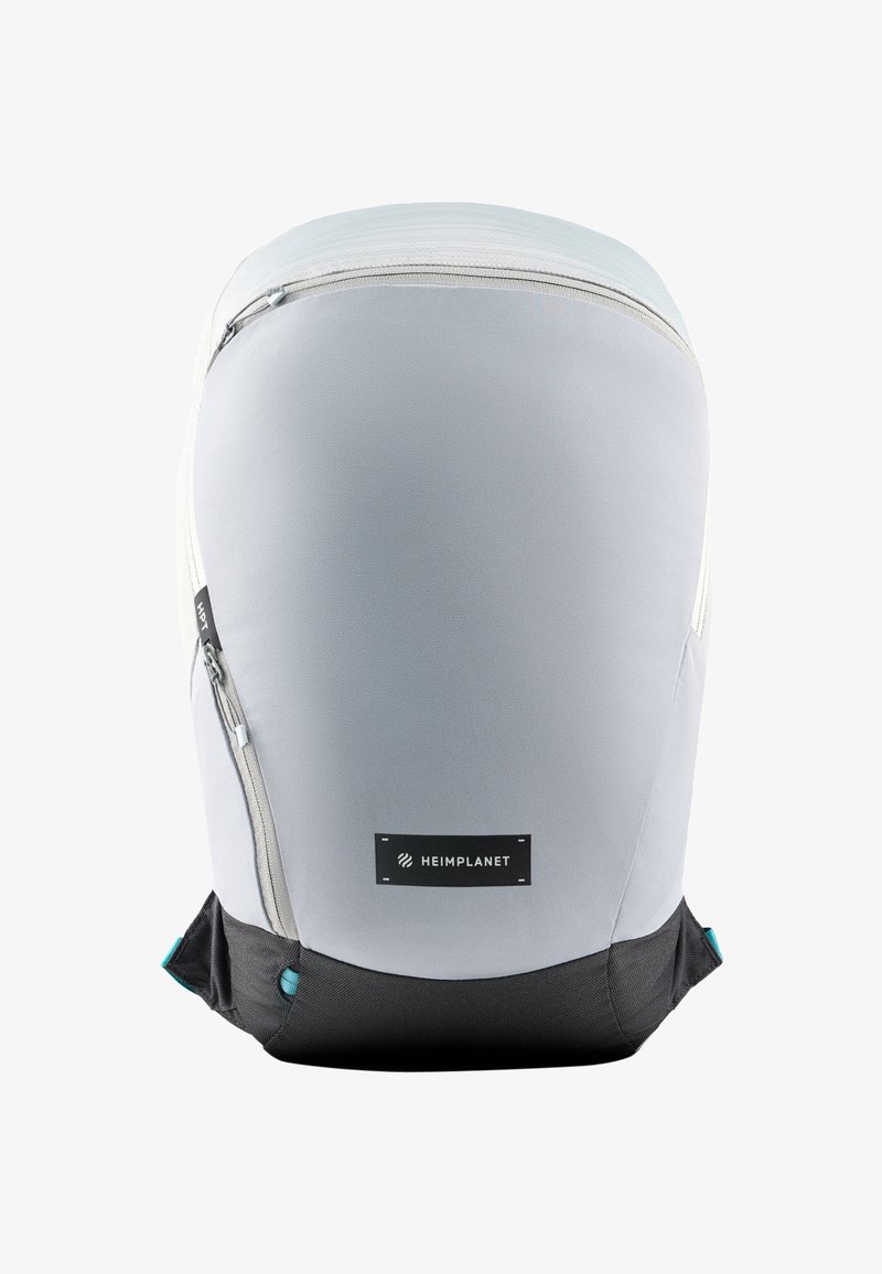 Mochila gris y negra con una textura suave, forma curva, cremallera lateral y un parche con el logotipo prominente en la parte frontal.