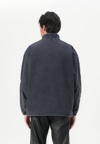 Casaco de ganga em cinza escuro com um corte descontraído, gola alta e punhos elásticos. Apresenta costuras visíveis e um design simples, sem adornos.
