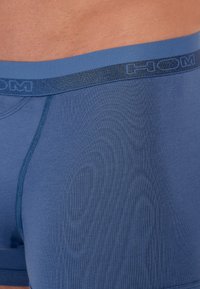 Niebieskie slipy typu boxer wykonane z miękkiej tkaniny o dopasowanym kroju. Posiadają kontrastowy, ciemny pas z nazwą marki "HOM" tkana w materiał.