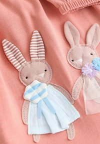 Baumwollkleidung in sanftem Rosa mit zwei Hasen-Applikationen, einer mit gestreiften Ohren und einem blauen Kleid, der andere mit pastellfarbenen Akzenten und Spitzenapplikationen.