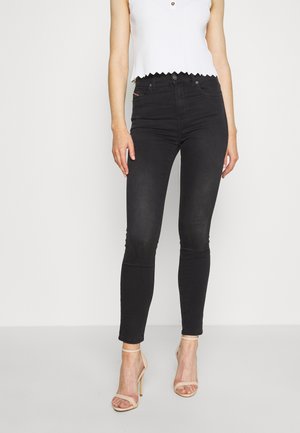 Smaltsiddende sorte jeans kombineret med en hvid ærmeløs top og beige højhælede sandaler på en ensfarvet baggrund.