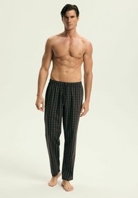 Czarne piżamowe spodnie w kratę z białym wzorem siatki, elastyczny pas, luźny krój i lekki materiał, noszone na boso.