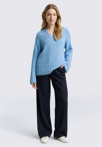 Hellblauer, flauschiger Pullover mit V-Ausschnitt, gerippten Bündchen und Saum, kombiniert mit dunklen, weit geschnittenen Hosen und weißen Sneakern. Gepflegter Casual-Look.