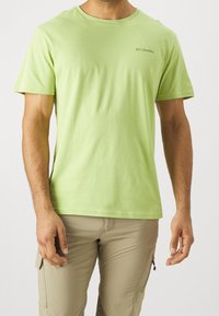 Světl zelené tričko s krátkým rukávem vyrobené z měkkého materiálu. Má kulatý výstřih a malé logo Columbia na levé horní části hrudníku.