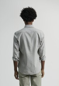 Camisa de manga larga a rayas grises y blancas con mangas remangadas y cuello recto, con una tela suave y texturizada.