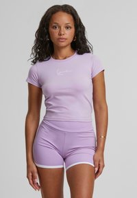 T-shirt viola aderente con maniche corte e un logo bianco, abbinato a pantaloni corti a vita alta dello stesso colore con rifiniture bianche. Tessuto dalla texture liscia.