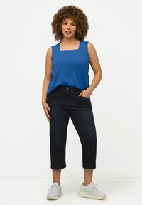 Top azul sin mangas con escote cuadrado, combinado con jeans oscuros y zapatillas claras. El conjunto presenta un corte holgado y una textura suave.