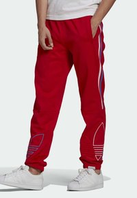 Red sweatpants with white and blue side stripes, elastic waistband, side pockets, and blue embroidered logo detail at the hem.