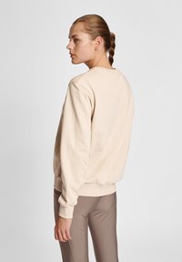 Beige sweatshirt med en afslappet pasform, rund halsudskæring og ribbede manchetter. Den er lavet af blødt materiale og har en glat tekstur.